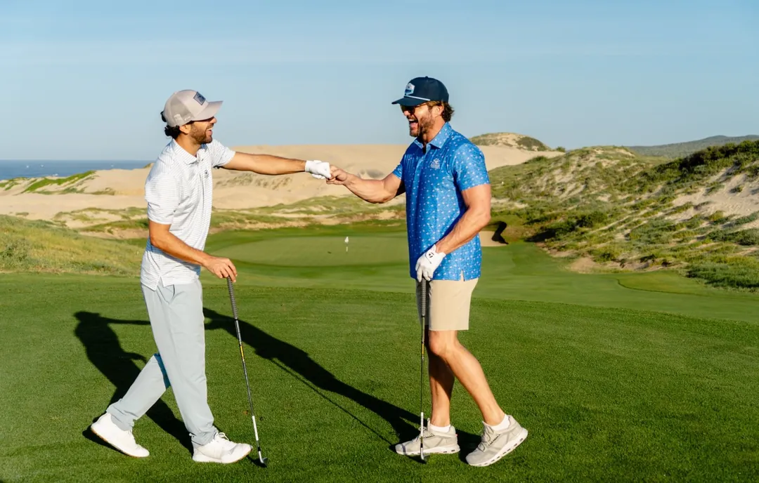 Two golfers bumping fists on a dune course above the Pacific